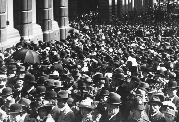 Crowds fill Martin Place to attend the official opening of the Commonwealth Bank. Construction of the head office building was completed in 1916 with the official opening taking place on 22 August. Inside the bank, speeches were made from a gallery overlooking the banking chamber. Looking down Martin Place to George Street a campaign for enlisting in the First World War may be seen. Of a population of 4 million a total of 416,809 Australians enlisted.