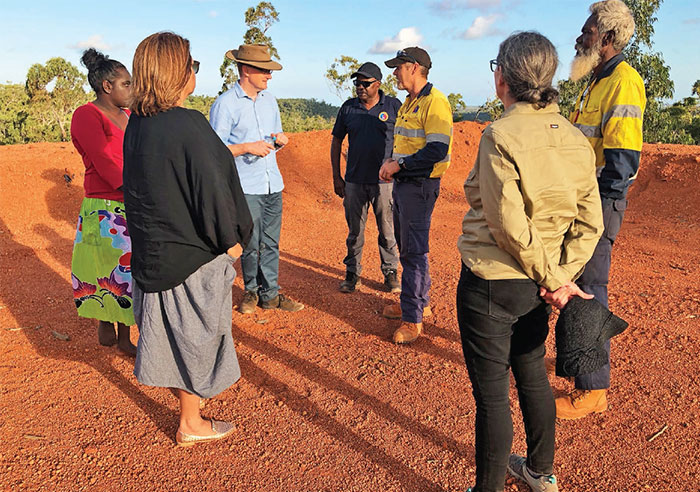A group of people standing in a circle in outback Australia on bare soil.