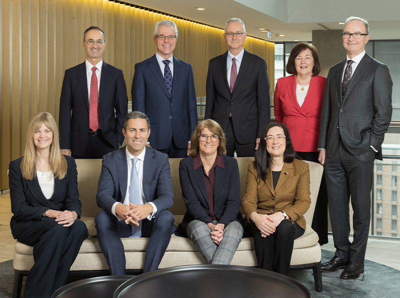 Group photograph of the Payments System Board members, all are smiling and looking directly at the camera. Four members are seated and five members are standing behind them. The order in which the members are sitting and standing and other details are set out in the caption below the photograph.