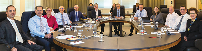 The Reserve Bank Board with members of staff; (clockwise from centre) Board members Governor Philip Lowe, Deputy Governor Guy Debelle, Catherine Tanna, Treasury Secretary Philip Gaetjens, Ian Harper, Carol Schwartz AM, Anthony Dickman (Reserve Bank Secretary), Mark Barnaba AM, Wendy Craik AM, Allan Moss AO; staff members: Christopher Kent (Assistant Governor, Financial Markets) and Luci Ellis (Assistant Governor, Economic); (back row) Andrea Brischetto (Deputy Secretary), Alex Heath (Head of Economic Analysis Department) and Ellis Connolly (Deputy Head of Domestic Markets Department), August 2018