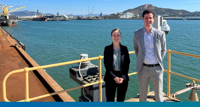 A young woman and gentleman are standing on a wharf, dressed in business suits, at the port of Townsville.