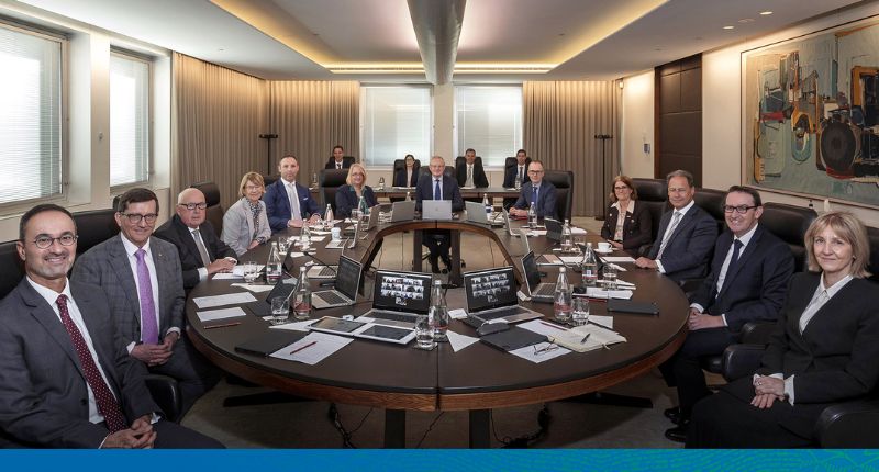 Photo of the Reserve Bank Board members sitting around the large oval board room table, smiling, and looking at the camera.