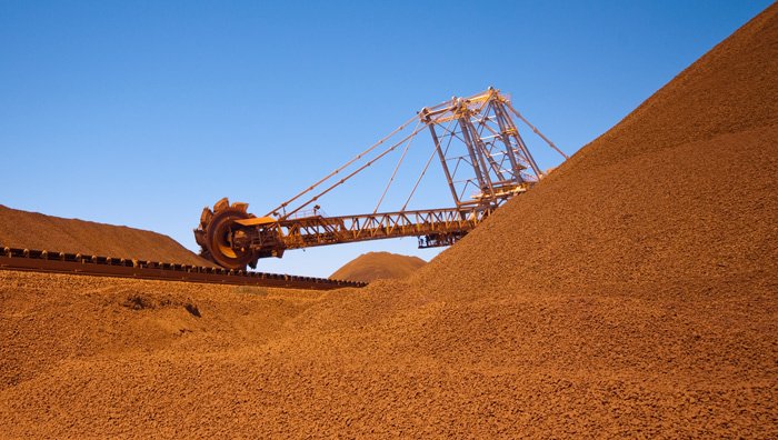 Heavy mining equipment sits among large piles of red earth