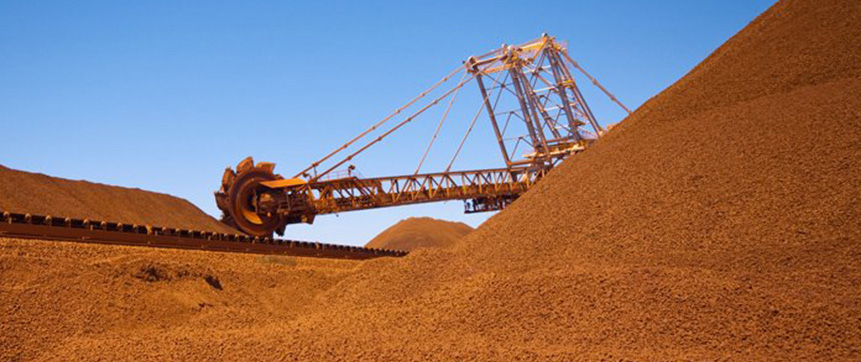 Heavy mining equipment sits among large piles of red earth