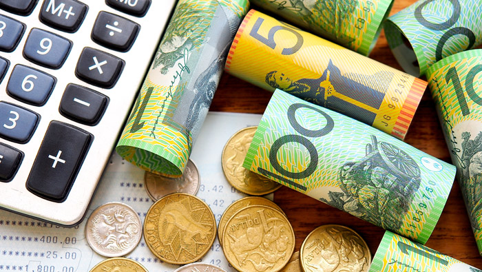 Rolled-up banknotes, coins and desktop calculator are sitting on a desk.