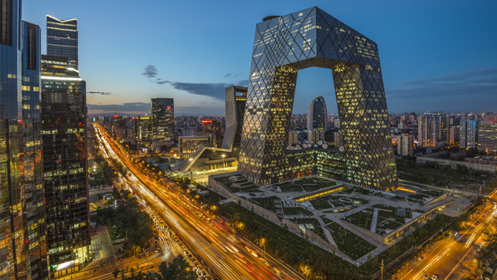 An A-shaped illumniated building dominates the skyline of a city at night.