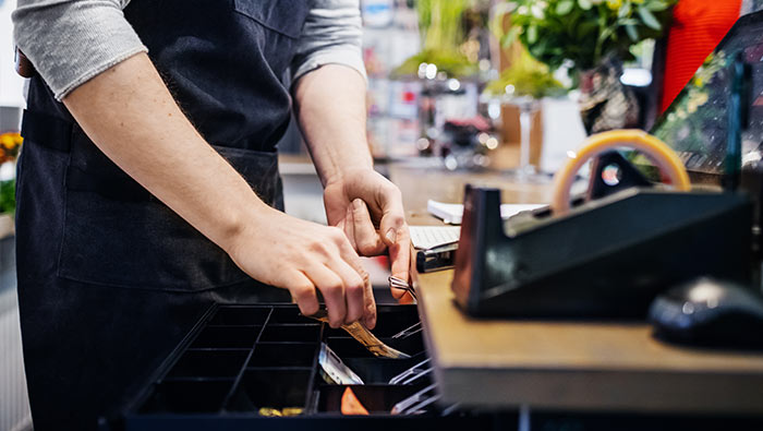 The hands of a cashier retrieve banknotes from a till