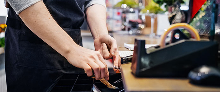 The hands of a cashier retrieve banknotes from a till