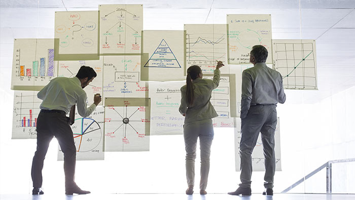 Three employees work on large charts stuck to a transparent wall