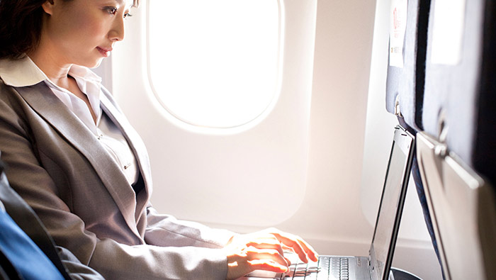 A woman aboard a plane types on her laptop.