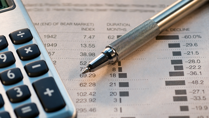 A pen and calculator lie on top of a financial newspaper