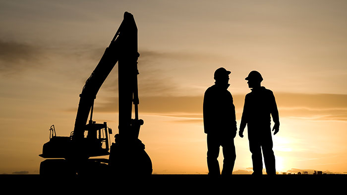 The outlines of two miners and an excavator against a sun setting.