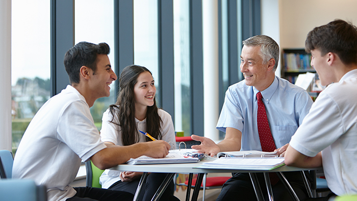 An older male employee sits at a table talking to his younger colleagues.