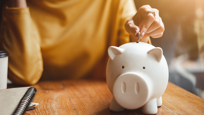 The hand of a woman inserts a coin into a piggy bank.