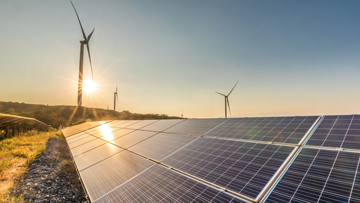 The sun rises behind windmills and solar panels.