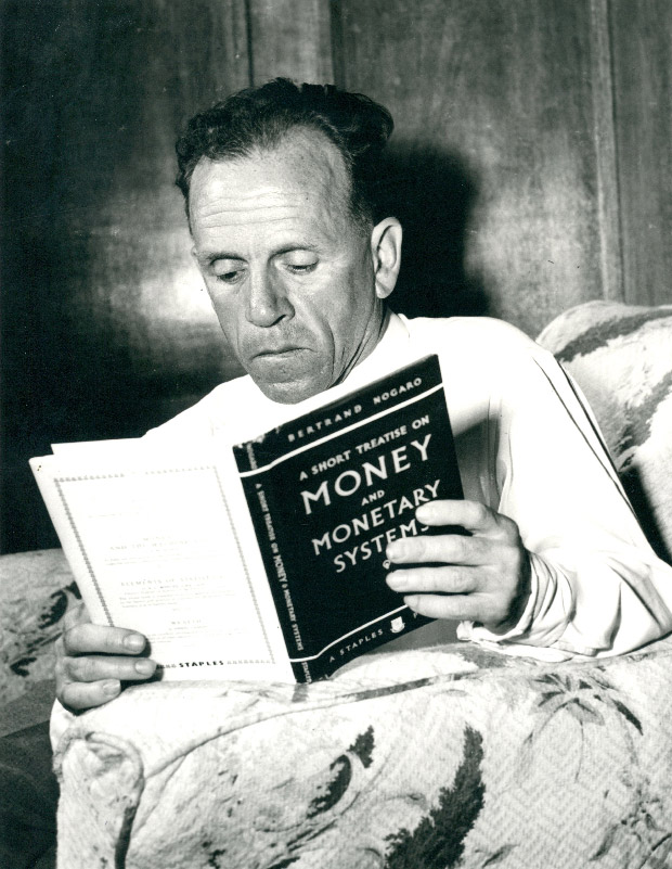 Archival photo of Dr HC Coombs in a lounge chair reading a book 'A Short Treatise on Money and  Monterary Systems'.