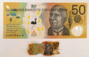 An undamaged $50 banknote is compared against a heat-affected $50 banknote. The shrunken $50 banknote is 1/10th the size compared to the sample banknote.