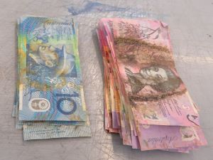 Two piles of discoloured banknotes. $10 blue banknotes with yellow stains and markings and $5 pink banknotes with dark brown stains and marking in the centre.