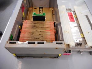 A metal box (ATM canister) filled halfway with $20 banknotes. Black mould stains the edges of the stacked banknotes.