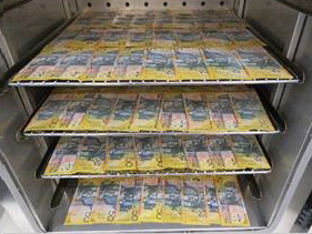 $50 banknotes laid across four metal racks in a dehumidifier for drying.