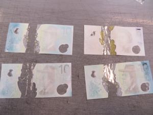 Damaged $10 banknotes placed horizontally side by side on a dark background. The banknotes have a bleached white appearance. Little of the original banknote colour and details remain.