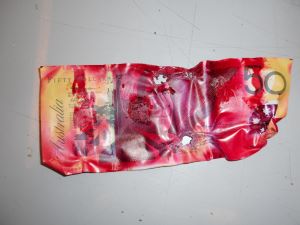 A $50 banknote stained in dark red ink by the anti theft device. The banknote has some puncture holes and shrunken edges and corners.