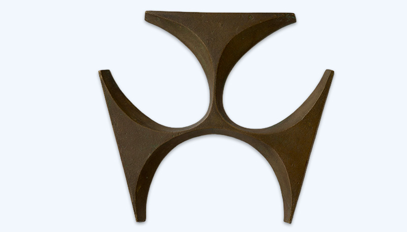 Photo of the RBA logo in bronze gun metal. The logo is an abstract geometric shape similar to a jigsaw piece. It has three curved shapes that are arranged symmetrically. The shapes join in the middle. Each is thin at the middle and then thicken to a flat straight edge as they branch out.